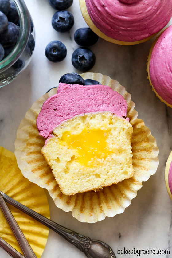 Moist and fluffy homemade lemon cupcakes with fresh lemon curd filling and blueberry buttercream frosting recipe from @bakedbyrachel A fun treat for any spring or summer occasion!