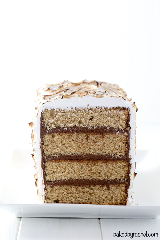 Front image of sliced s'more cake. Layers of cinnamon graham cake with chocolate buttercream filling and coated in toasted marshmallow frosting